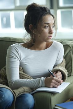 a woman sitting on a couch with a pen in her hand and looking off to the side