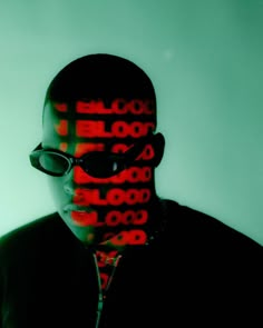 a man wearing glasses and a jacket with the word blood on it's face