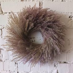 a dried wreath on a brick wall with white bricks in the background and brown grass hanging from it's center