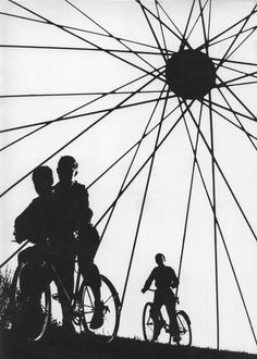 two people riding bikes next to each other under a large spoke wheel with the sky in the background