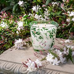 a glass candle sitting on top of a cement block surrounded by flowers and greenery