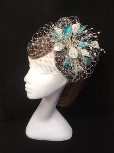 Teal blue and silver veiled fascinator perfect for the guest who wants something beautifully unique. This design is a beautiful selection of glass effect leaves and flowers clustered together amongst a fine layer of veiling and set onto a fine comfort base tiara band. As with all our designs, this piece can be made exact to the image or in any colour combination to match in with your outfit. If a specific colour is required customers can message over an image of their outfit and accessories, or Formal Blue Fascinator With Handmade Flowers, Elegant Blue Headpiece With Handmade Flowers, Blue Headband With Handmade Flowers, Blue Handmade Flowers Headband, Elegant Blue Fascinator With Handmade Flowers, Silver Costume Hats And Headpieces For Kentucky Derby Wedding, Blue Handmade Flower Hair Accessories For Weddings, Silver Mini Hat For Wedding And Kentucky Derby, Silver Mini Hats For Kentucky Derby And Weddings