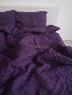 an unmade bed with purple sheets and pillows