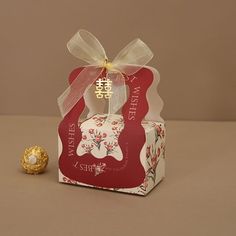 a small red box with a white bow on it and a gold ball in front