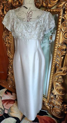 a white dress on display in front of a gold framed mirror and ornately decorated wall