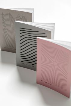 three different colored books on a white surface with wavy lines in the middle and bottom