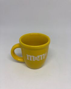 a yellow coffee cup with the word m & m on it's side sitting in front of a white background