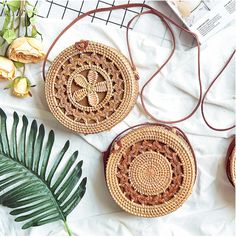 three round woven purses sitting on top of a white sheet next to plants and flowers