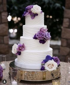 a wedding cake with purple and white flowers on the top is sitting on a table