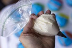 a hand holding a piece of cake in front of a plastic container with icing on it