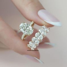 a woman's hand holding two rings with diamonds on them and one is wearing a white manicure