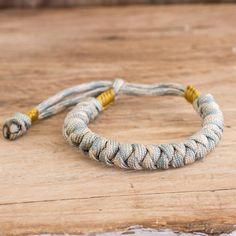 a rope bracelet with two yellow beads on top of a wooden table next to a bottle