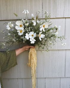 a person holding a bouquet of flowers in front of a wall with white and yellow flowers