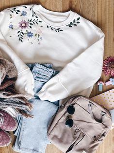 an assortment of clothing and accessories laid out on top of a wooden floor next to a purse