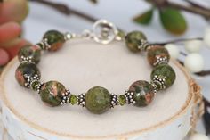 Add a touch of earthy sparkle to your look with this green & coral unakite gemstone bracelet. It features faceted beads that add texture & a touch of pizazz accented with crystal & sterling silver. All our items are handmade with care to provide you with a piece of wearable art. SIZE Length is 7 3/4 inches long Width is 10mm MATERIALS 10mm Faceted Unakite 4mm Crystal Sterling Silver Bead Caps 3mm Sterling Silver Balls Sterling Silver Toggle Green Gemstone Bracelet, Diy Bracelets Easy, 925 Silver Bracelet, Boho Green, Coral Jewelry, Handmade Jewelry Diy, Silver Bead, Green Gemstones, Sterling Silver Bracelet