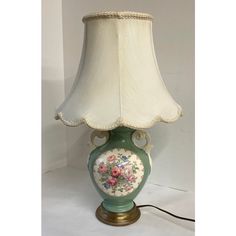 a green vase with flowers painted on it and a white lamp shade sitting on top of it