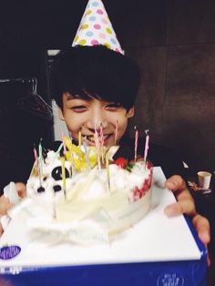 a young boy is smiling and holding a birthday cake with candles on it in front of his face