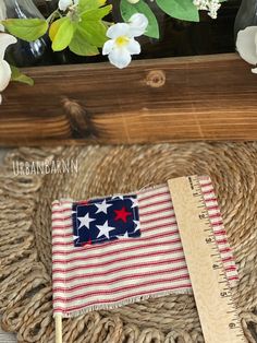 an american flag on a straw mat next to a ruler and flower pot with white flowers in the background