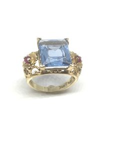 This gorgeous blue topaz ring in 14k yellow gold is perfect for the december born. The stunning emerald cut center stone is flanked by 2 flowers with sparkling ruby red spinel on each side. This vintage ring is in amazing shape. A lot of these rings are part of the jewelry collection of a 92 year old collector and in great condition.Metal: 14k goldWeight: 4.9 gmsGemstones: Blue Topaz, Ruby Red SpinelGemstone Size: 12 x 10mmRing Size: 5All jewelry comes boxed ready for gift giving.LAYAWAY AVAILAB Formal Yellow Gold Blue Topaz Ring, Yellow Gold Rings With Blue Topaz And 17 Jewels, Formal Gold Birthstone Ring With Blue Topaz, Formal Yellow Gold Topaz Birthstone Ring, 14k Gold Fine Jewelry Topaz Ring Hallmarked, Fine Jewelry 14k Gold Hallmarked Topaz Ring, 14k Gold Hallmarked Fine Jewelry Topaz Ring, Hallmarked 14k Gold Topaz Ring, Fine Jewelry, Formal Hallmarked Blue Topaz Birthstone Ring