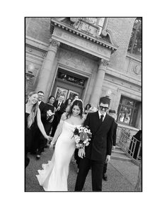 black and white photograph of bride and groom walking down the street in front of an old building