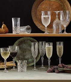 several wine glasses are lined up on a shelf next to an old plate and pears