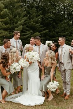 a group of people standing around each other in front of trees and grass with white flowers