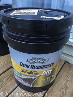 a bucket of deck resurfacer sitting on top of a wooden table next to a window