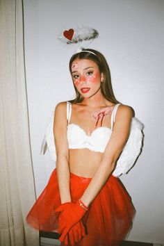 a woman in a red skirt and white bra top with wings on her head posing for the camera