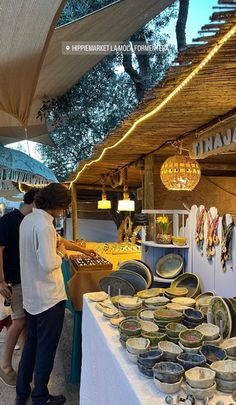 people are shopping at an outdoor market with plates and bowls on the table in front of them