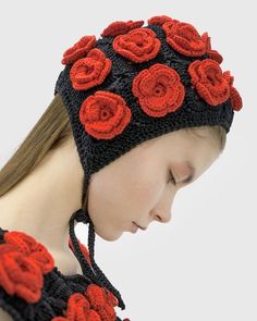 a woman wearing a crocheted hat with red flowers on the front and sides