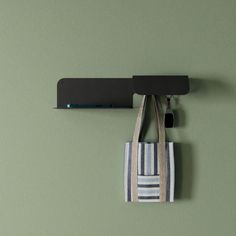 a bag hanging from a hook on a green wall with a black shelf above it