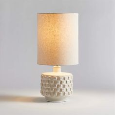 a white ceramic table lamp with a light shade on it's base and a beige fabric lampshade