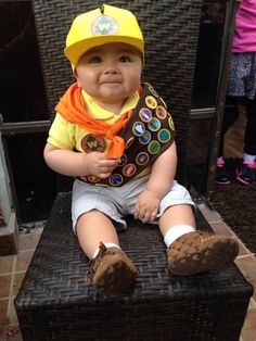 a baby sitting on top of a brown chair wearing a yellow hat and orange scarf