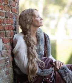 a woman with long hair sitting against a brick wall