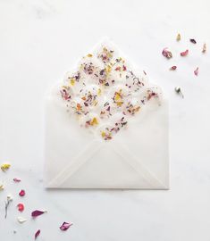 a white envelope with dried flowers in it and scattered petals around the envelope, on a marble surface