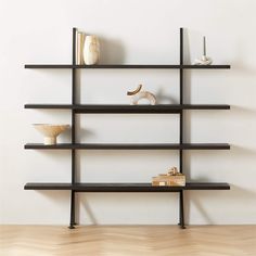 an empty shelf with books, vases and figurines on it in front of a white wall