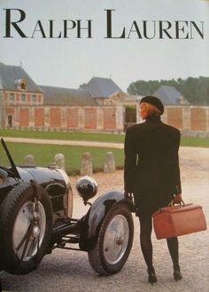 a woman in a black suit and hat holding a suitcase next to an old car