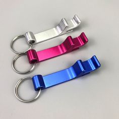 three different colored metal keychains on a white surface, one has a ring and the other has a clip