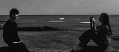 two people sitting on rocks near the ocean