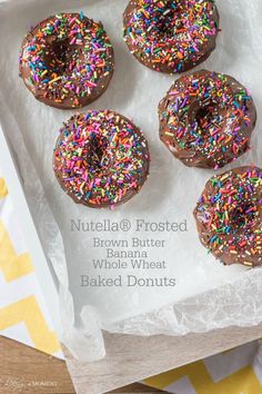 four chocolate covered donuts with sprinkles in a white paper wrapper