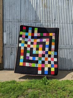 a black quilt with multicolored squares on it sitting in front of a building