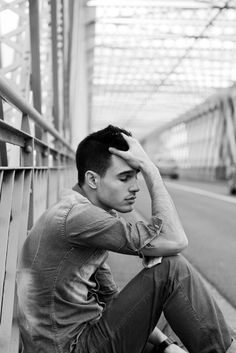 a young man sitting on the side of a road next to a train track with his head in his hands