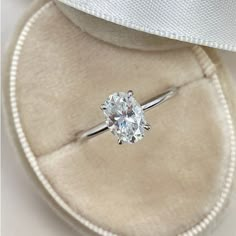 an engagement ring with a diamond in it sits inside a velvet box on top of a white cloth