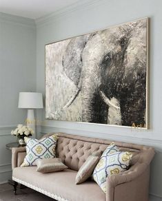 an elephant painting hangs on the wall above a couch with two pillows and a lamp