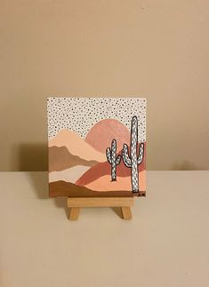 a small wooden easel with a cactus painting on it's side, sitting on a table