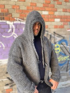 a man standing in front of a brick wall wearing a gray sweater and black pants