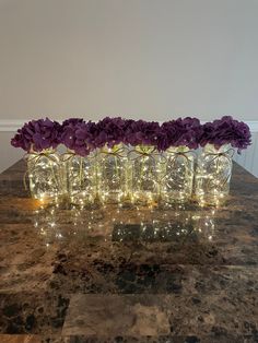 purple flowers are in glass vases with lights on the top and bottom, sitting on a marble table