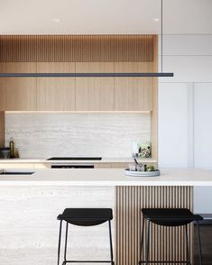 two stools are sitting at the bar in this modern kitchen with white countertops and wood paneling