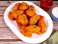 some fried food on a white plate next to a fork and sauce bottle with a spoon in it