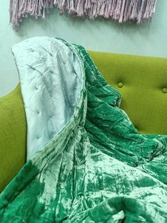 a green and white blanket sitting on top of a green couch next to a wall